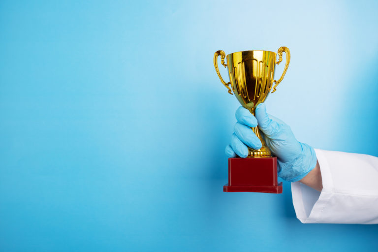 medical award, golden cup in doctor's hands on blue background, copy space